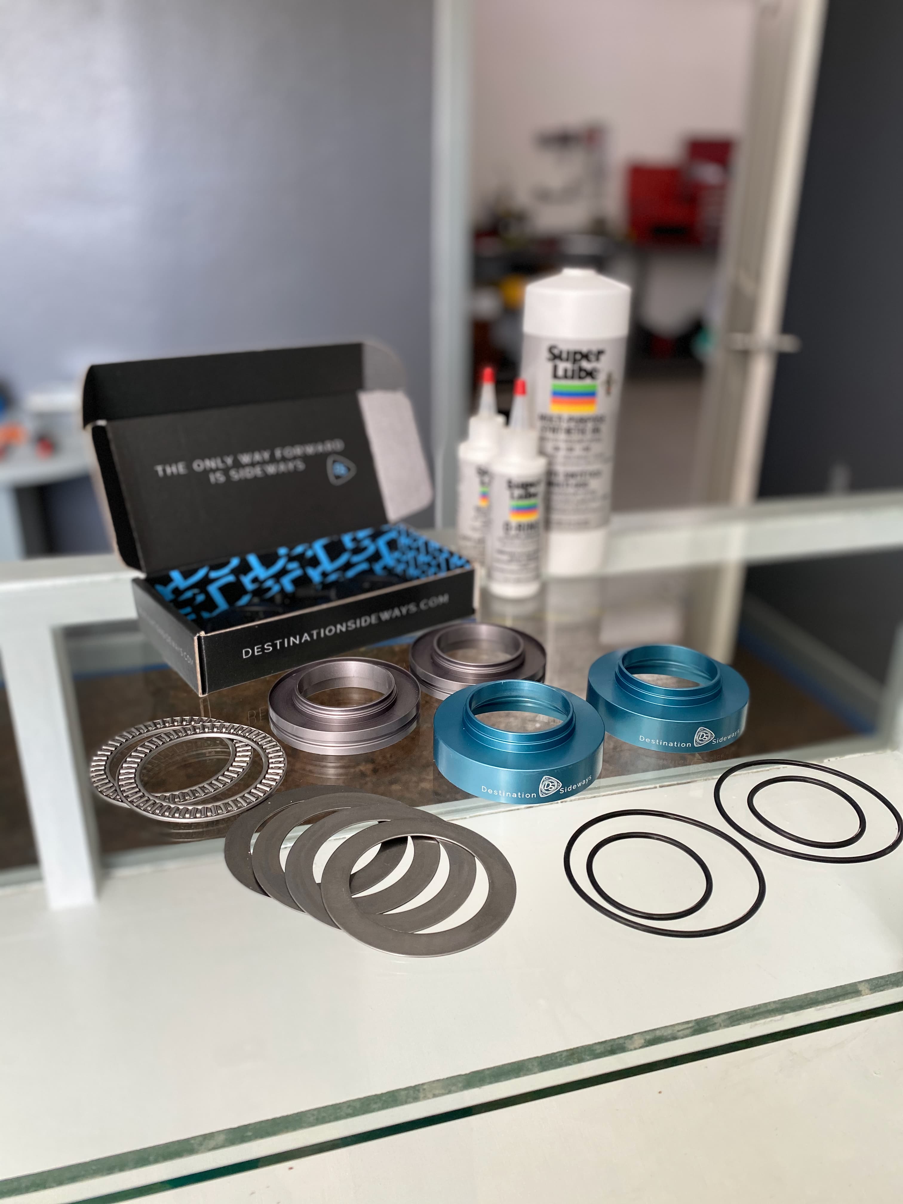 V1 adapter parts laid out on a counter: blue and silver housing halves, two needle bearings, thrust washers and o-rings, with the original box and two bottles of lubricant behind them.