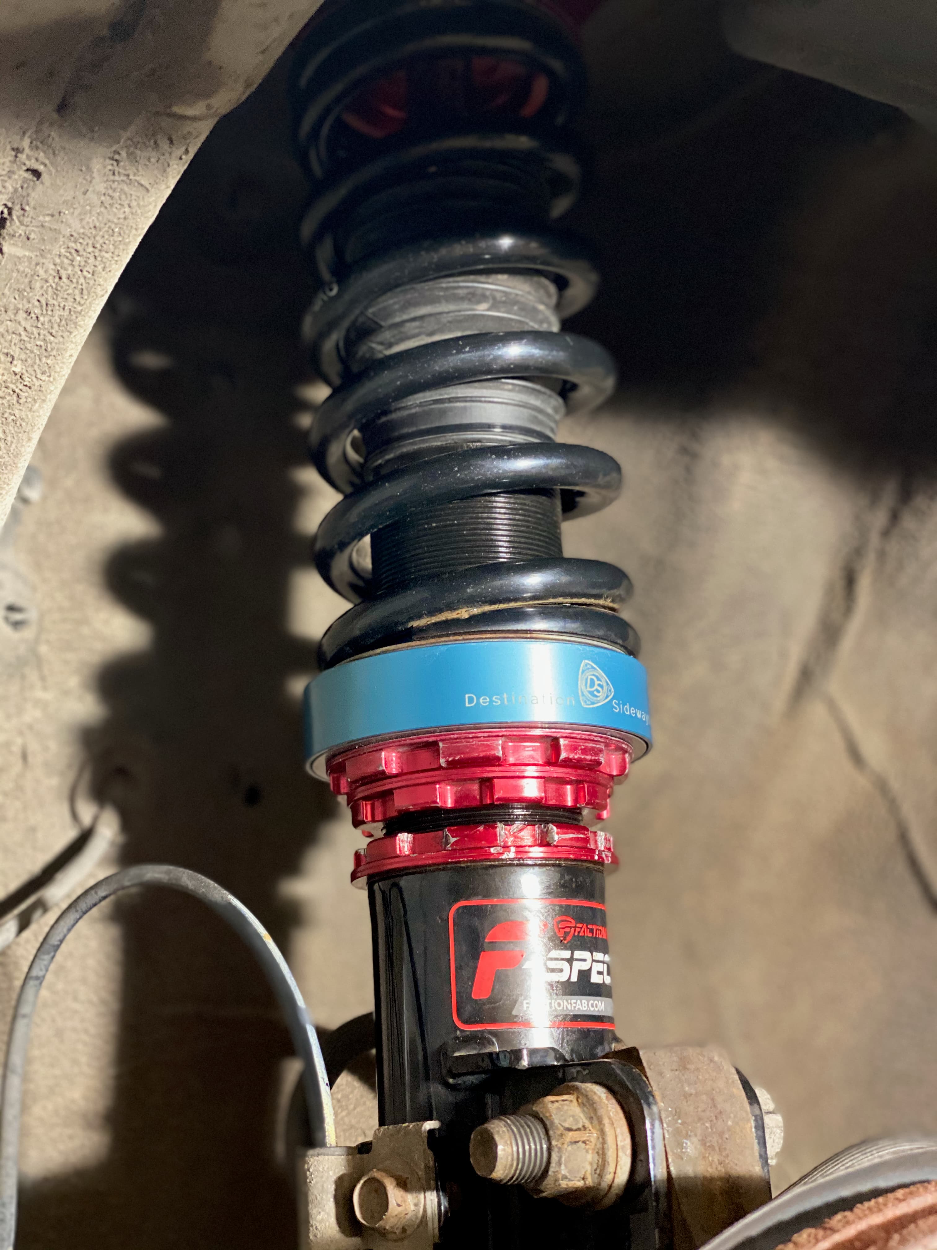 Close view of a V1 adapter installed between a black spring and the red lower perch of a coilover.