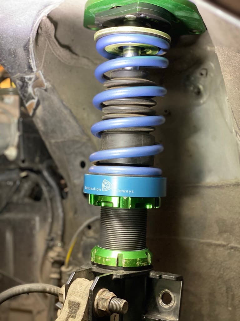 V1 adapter installed on a car, between the bottom of a blue spring and the green lower perch of the coilover.
