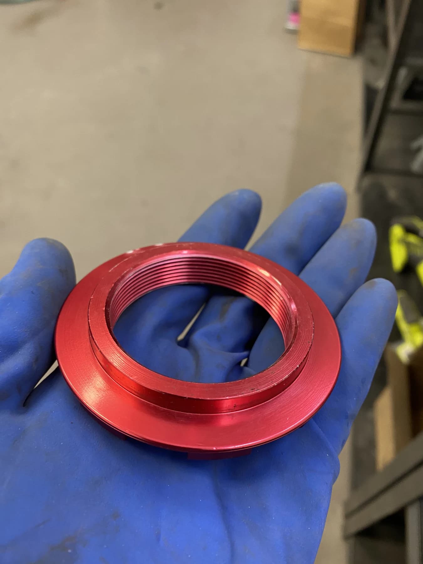Red spring perch collar held in a gloved hand, showing the raised circular lip whose outside diameter was ground for this V1 installation.