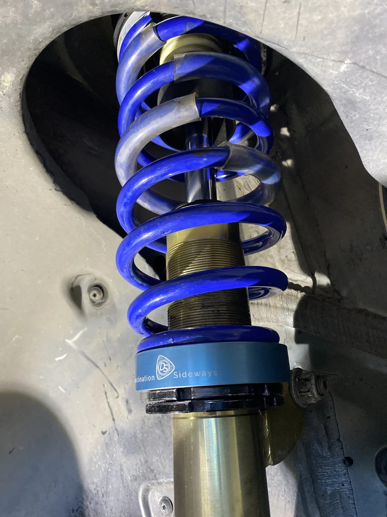 Blue V1 adapter below a blue spring above the black lower perch, installed inside a wheel well.
