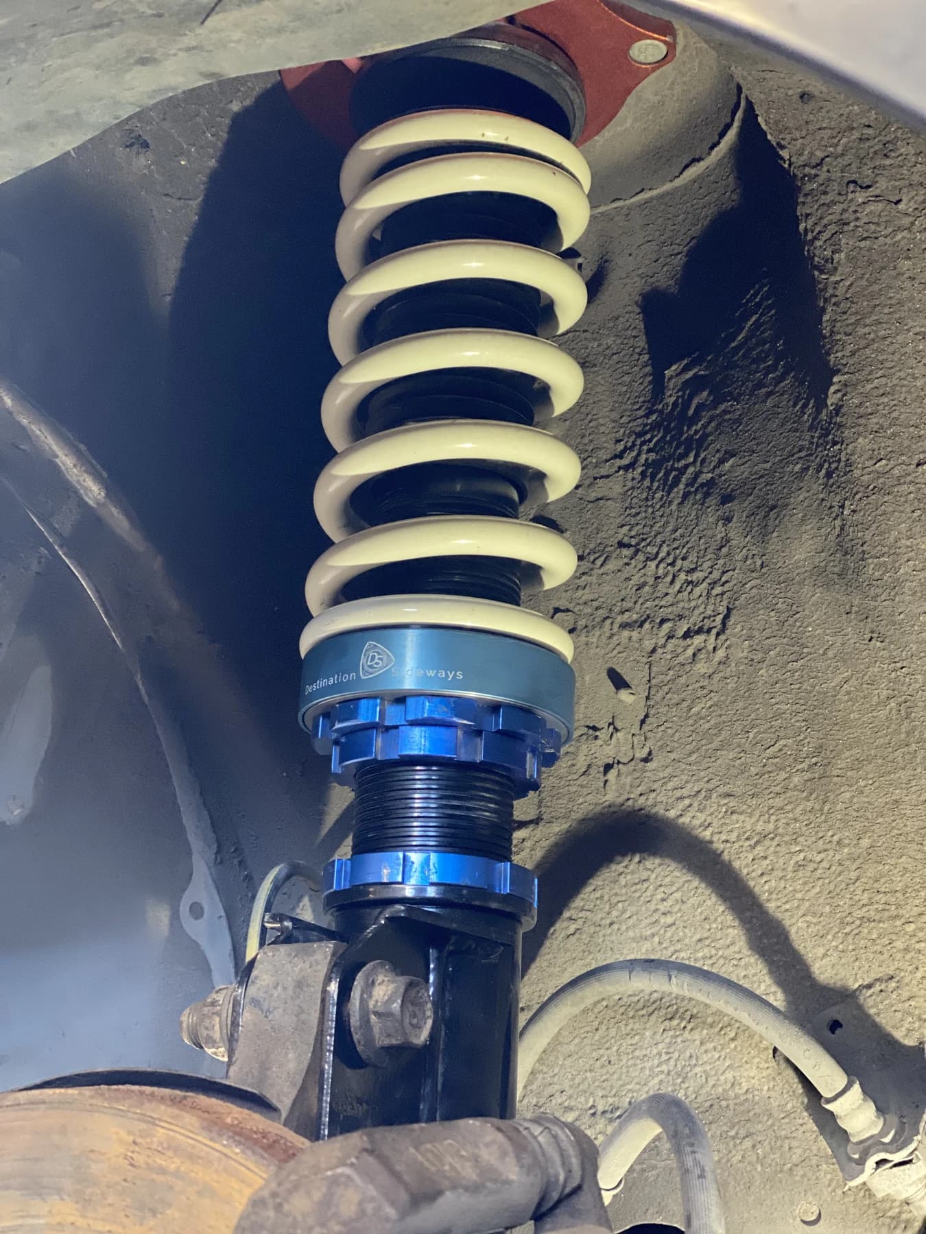 A blue adapter below a white spring on a coilover installed in a wheel well.