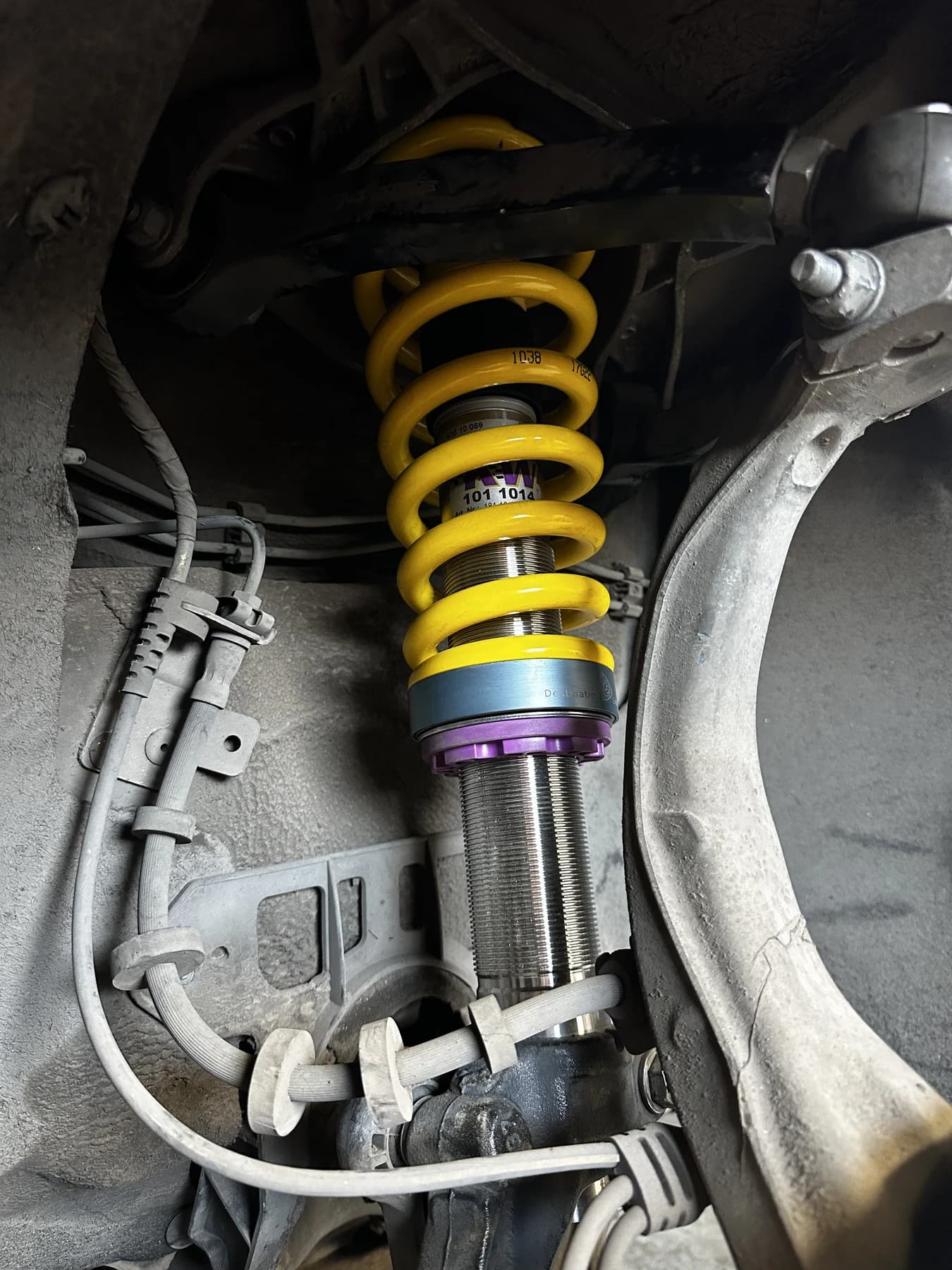 A coilover installed inside a wheel well, with a blue V1 adapter between a yellow spring and purple lower perch.
