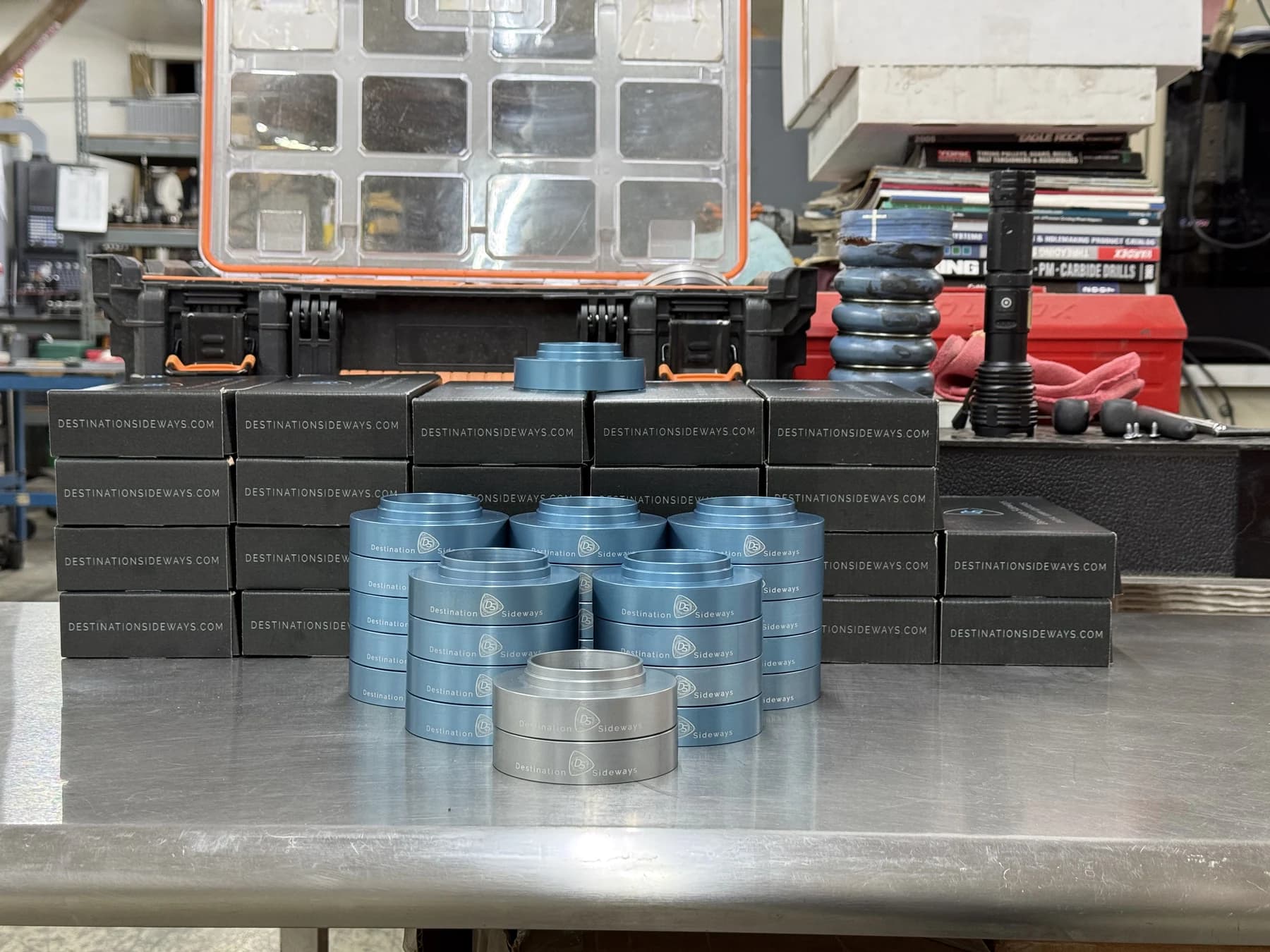 Stacks of blue and silver housings on a workbench in front of black boxes.