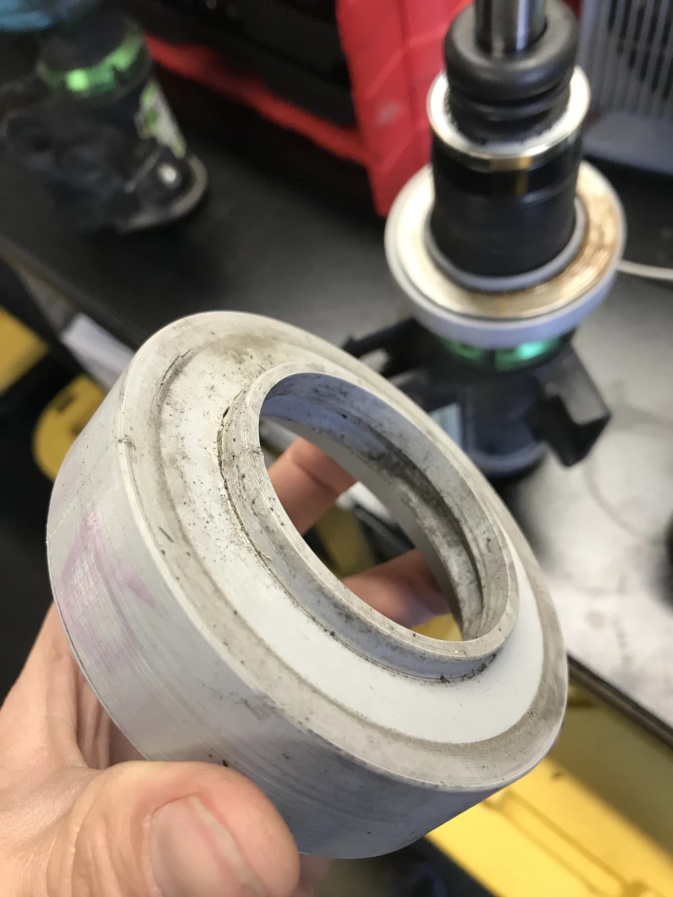 A pale printed housing held beside a disassembled coilover on the workbench.