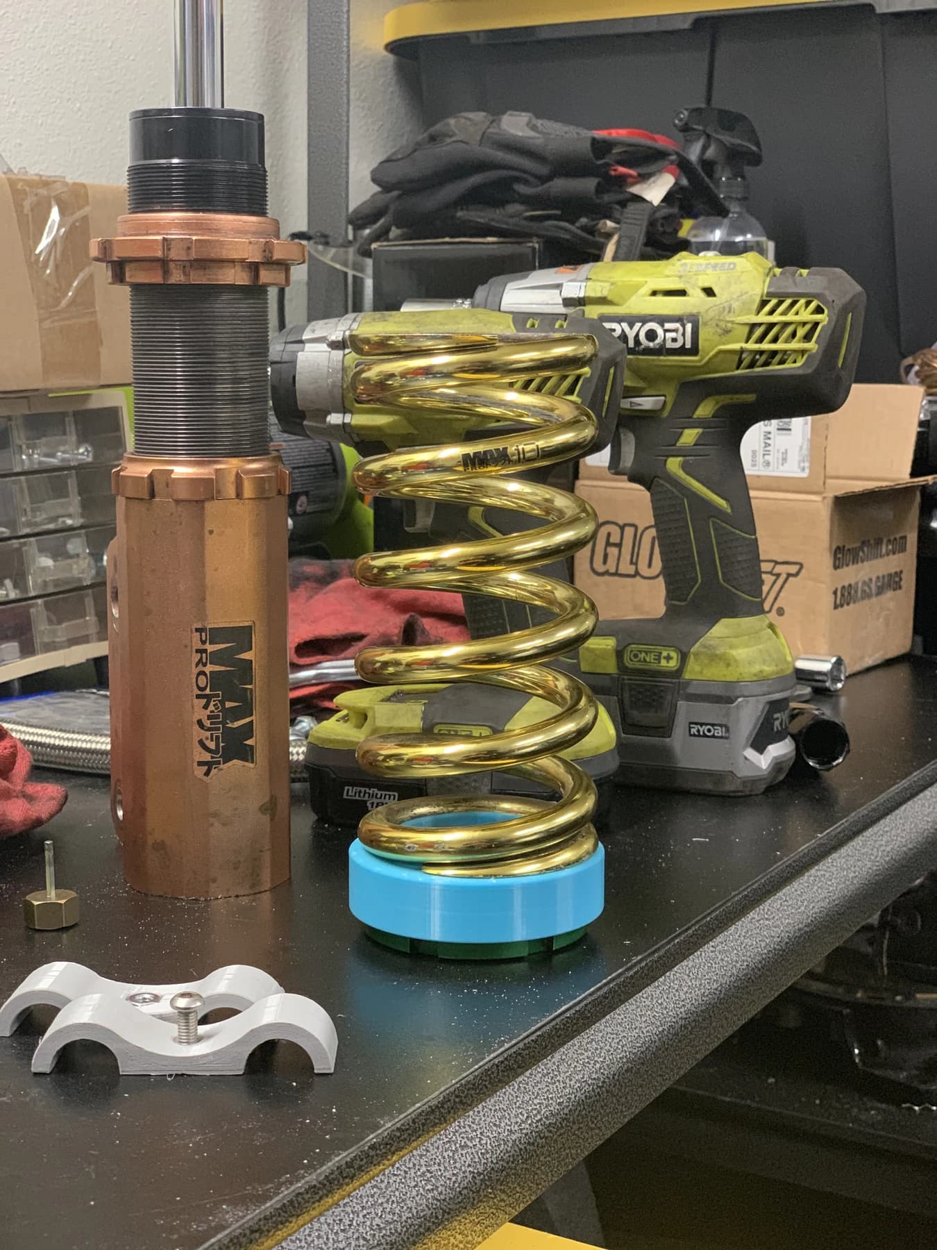 A gold spring with a blue adapter beside a disassembled coilover on the bench.